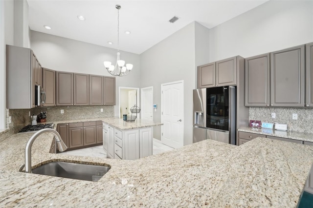 kitchen featuring stainless steel appliances, a towering ceiling, sink, a kitchen island, and light stone countertops