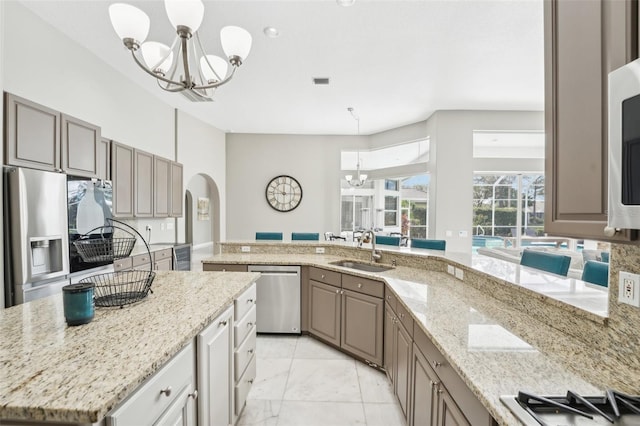 kitchen with light stone counters, stainless steel appliances, hanging light fixtures, sink, and a center island