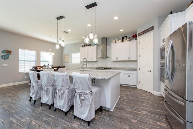 kitchen featuring appliances with stainless steel finishes, sink, wall chimney range hood, decorative light fixtures, and white cabinets