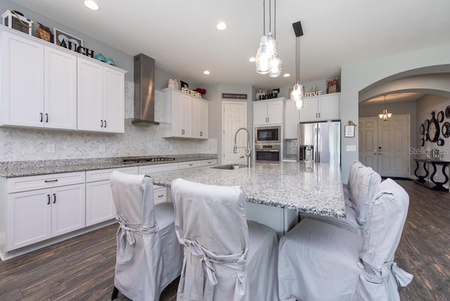 kitchen with sink, a center island with sink, wall chimney range hood, and appliances with stainless steel finishes