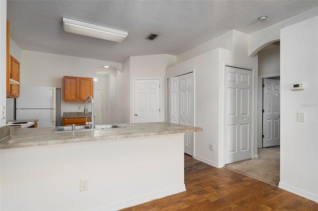 kitchen with dark wood-type flooring, kitchen peninsula, sink, white fridge, and a textured ceiling