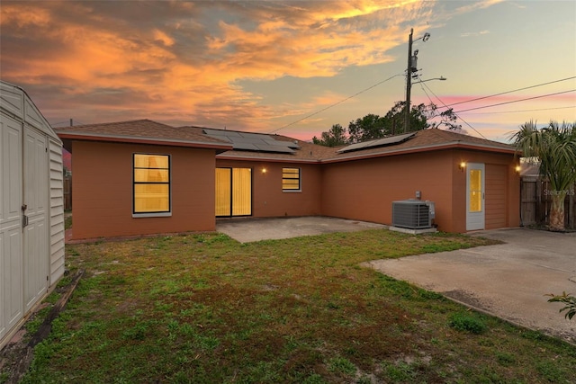 back house at dusk with cooling unit, a patio area, solar panels, and a yard