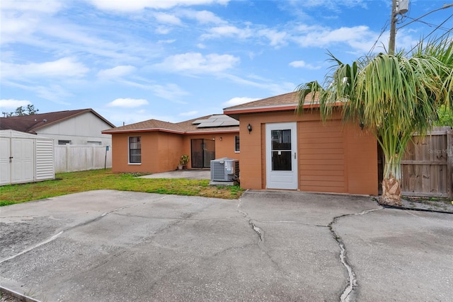 rear view of property featuring a lawn, a storage unit, a patio area, central AC, and solar panels