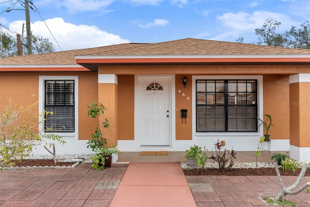 view of exterior entry with roof with shingles and stucco siding