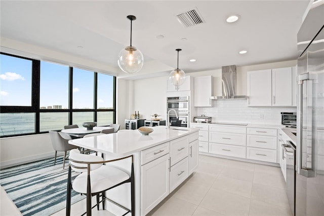 kitchen with wall chimney range hood, white cabinets, appliances with stainless steel finishes, a water view, and tasteful backsplash