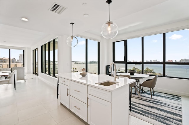 kitchen featuring a center island with sink, white cabinetry, sink, decorative light fixtures, and a water view