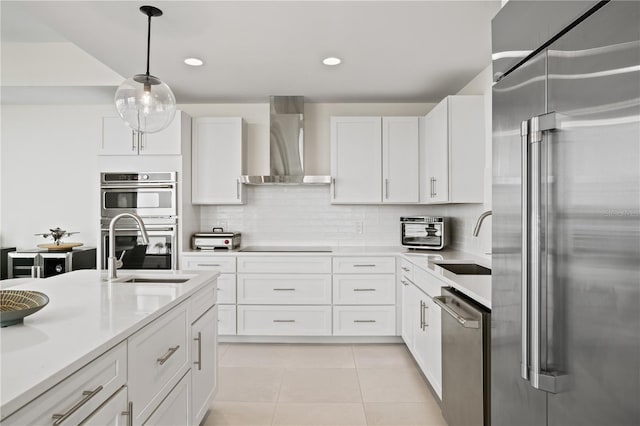 kitchen featuring wall chimney range hood, sink, pendant lighting, white cabinetry, and appliances with stainless steel finishes