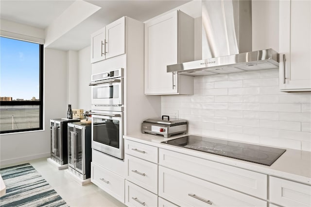 kitchen featuring backsplash, double oven, black electric cooktop, white cabinetry, and wall chimney exhaust hood