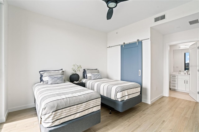 bedroom featuring connected bathroom, a barn door, light hardwood / wood-style flooring, and ceiling fan