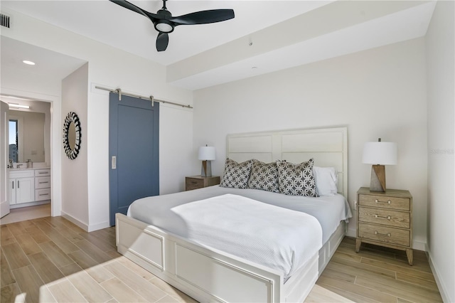 bedroom featuring connected bathroom, a barn door, light hardwood / wood-style flooring, and ceiling fan