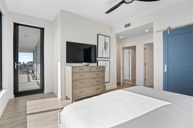 bedroom with ceiling fan, light hardwood / wood-style flooring, and a barn door