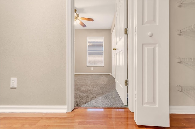 corridor with light carpet, light wood finished floors, and baseboards