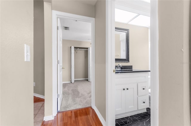 hall with visible vents, a sink, baseboards, and wood finished floors