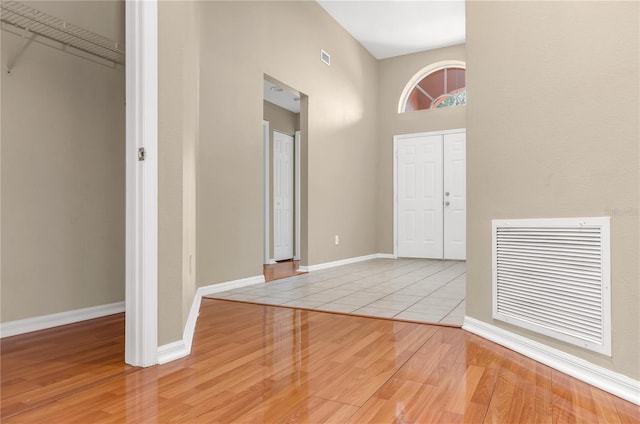 foyer featuring a high ceiling, visible vents, baseboards, and wood finished floors