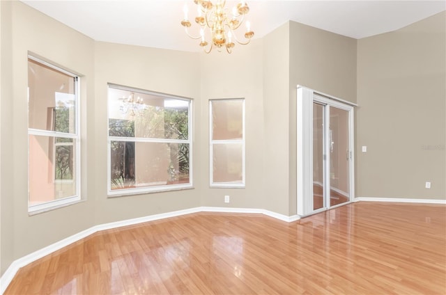 empty room with an inviting chandelier, baseboards, and wood finished floors