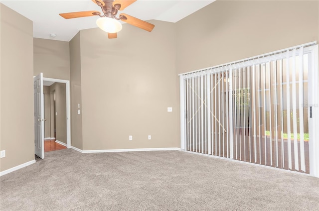 spare room featuring carpet floors, ceiling fan, a towering ceiling, and baseboards