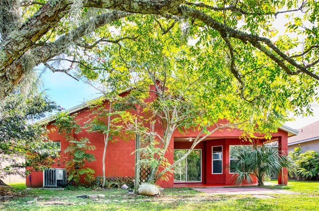 rear view of property with cooling unit, stucco siding, and a lawn