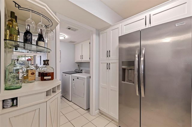 kitchen featuring stainless steel fridge, white cabinetry, light tile patterned floors, and washer and clothes dryer