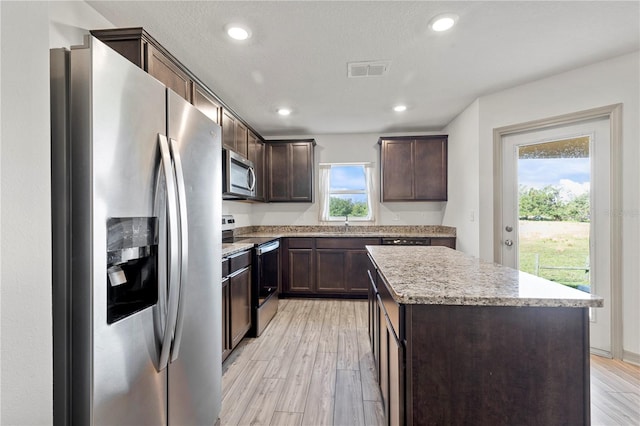 kitchen featuring a center island, dark brown cabinetry, a textured ceiling, light wood-type flooring, and appliances with stainless steel finishes