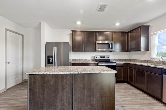 kitchen with sink, appliances with stainless steel finishes, dark brown cabinets, a center island, and light wood-type flooring