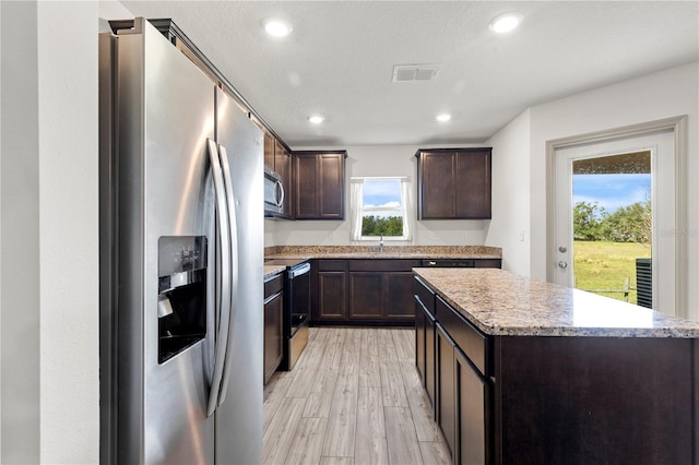 kitchen featuring light hardwood / wood-style flooring, a textured ceiling, a kitchen island, dark brown cabinets, and appliances with stainless steel finishes