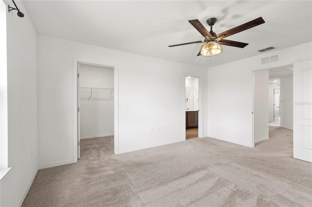 unfurnished bedroom featuring ensuite bath, light carpet, ceiling fan, a walk in closet, and a closet