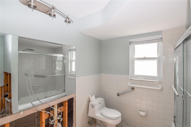 bathroom featuring tile walls, toilet, and a shower with shower door