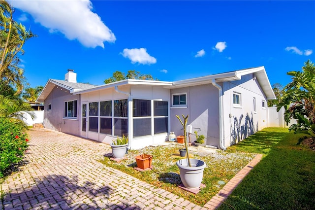 back of property featuring a lawn, a sunroom, and a patio area