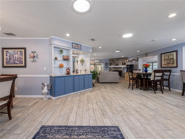 interior space featuring crown molding, a fireplace, a textured ceiling, and light wood-type flooring