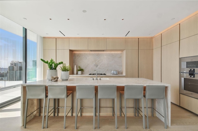 kitchen featuring light brown cabinetry, oven, an island with sink, and a kitchen breakfast bar