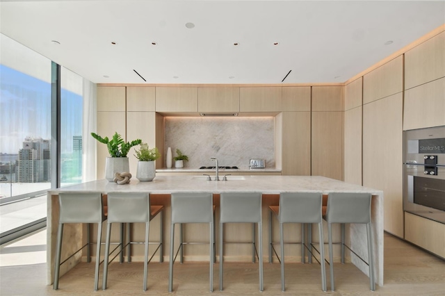 1000 Water St Unit 1702, Tampa, FL 33602 - kitchen featuring a kitchen island with sink, tasteful backsplash, light stone countertops, light brown cabinetry, and a kitchen breakfast bar