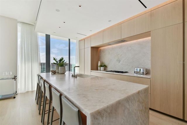 kitchen with light hardwood / wood-style flooring, sink, a center island with sink, and a wall of windows