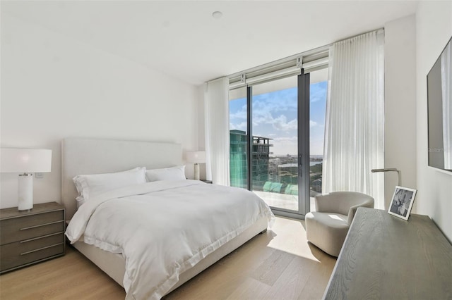 bedroom featuring access to exterior, light wood-type flooring, and floor to ceiling windows