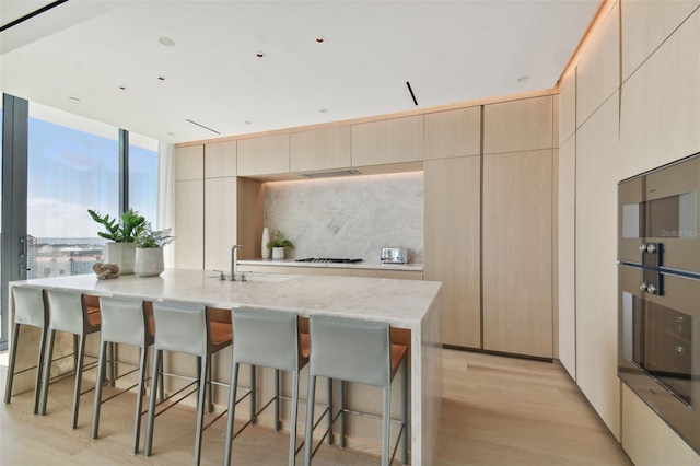 kitchen featuring a kitchen island with sink, light hardwood / wood-style floors, sink, and light stone counters