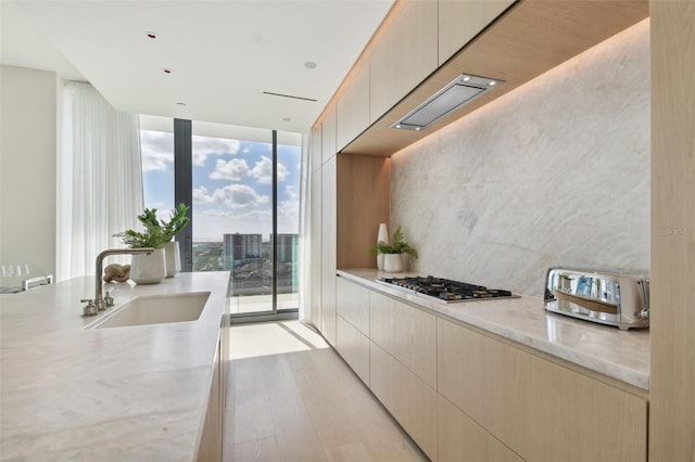 kitchen featuring light hardwood / wood-style floors, stainless steel gas stovetop, sink, a wall of windows, and light brown cabinetry