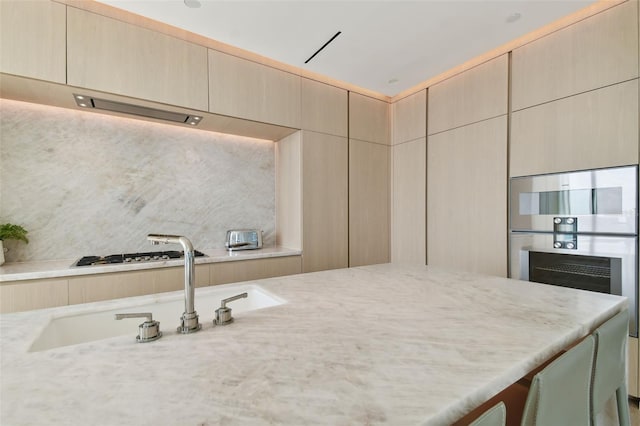 kitchen with sink, tasteful backsplash, light brown cabinetry, light stone countertops, and stainless steel gas stovetop