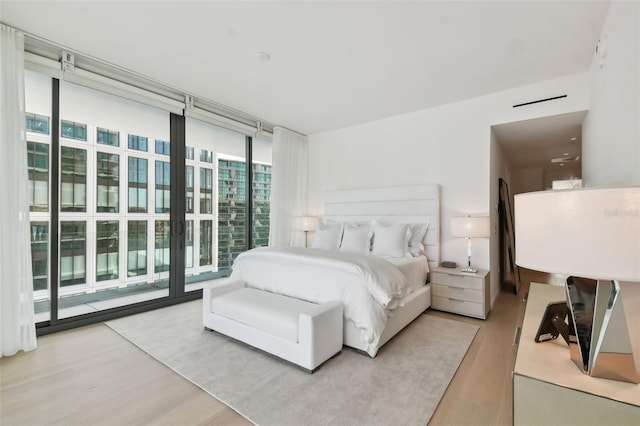 bedroom with access to exterior, light wood-type flooring, and floor to ceiling windows