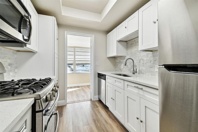 kitchen featuring white cabinetry, appliances with stainless steel finishes, a tray ceiling, and light stone countertops