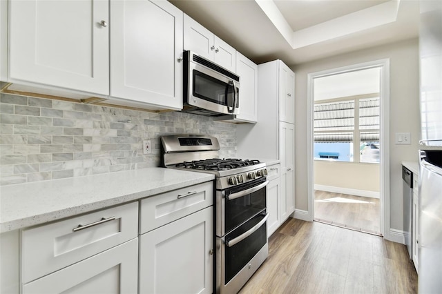 kitchen with appliances with stainless steel finishes, white cabinets, decorative backsplash, light stone counters, and light wood-type flooring