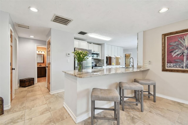 kitchen featuring backsplash, a breakfast bar, kitchen peninsula, white cabinetry, and stainless steel appliances