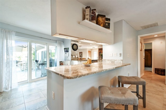 kitchen featuring a breakfast bar, kitchen peninsula, light tile patterned floors, and light stone counters