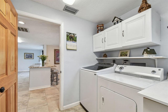 clothes washing area featuring light tile patterned flooring, cabinets, and washer and dryer