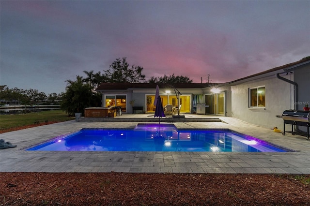 pool at dusk featuring grilling area, a jacuzzi, and a patio