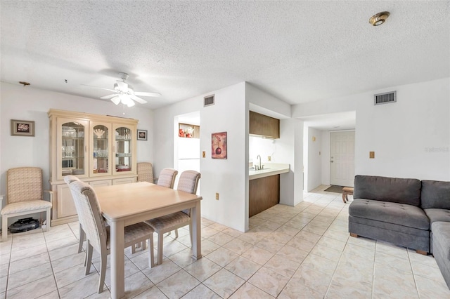 dining space with a textured ceiling, sink, light tile patterned flooring, and ceiling fan