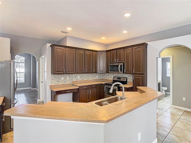 kitchen with appliances with stainless steel finishes, sink, an island with sink, dark brown cabinets, and tasteful backsplash