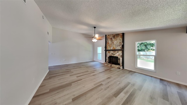 unfurnished living room featuring a textured ceiling, a fireplace, light hardwood / wood-style floors, and ceiling fan