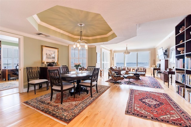 dining room featuring crown molding, hardwood / wood-style flooring, a raised ceiling, and a chandelier