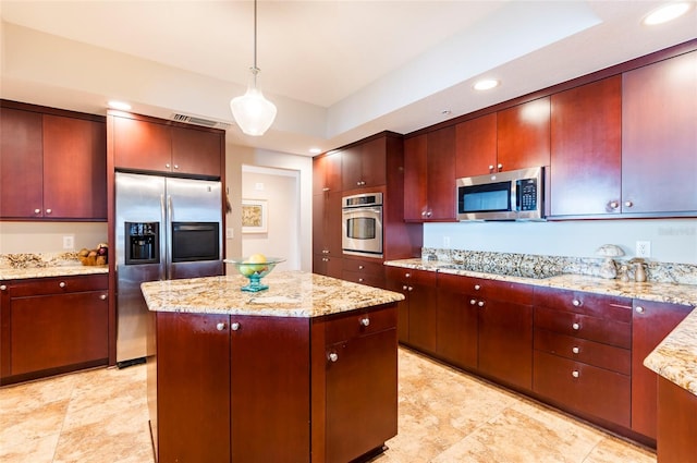 kitchen with light stone counters, appliances with stainless steel finishes, a center island, and decorative light fixtures