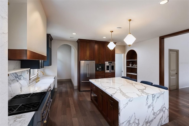 kitchen featuring light stone counters, appliances with stainless steel finishes, dark hardwood / wood-style floors, decorative light fixtures, and a center island