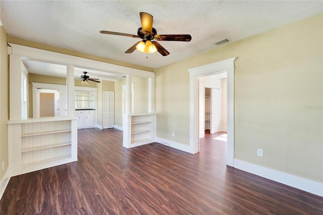 empty room with dark wood-style flooring, decorative columns, visible vents, a textured ceiling, and baseboards